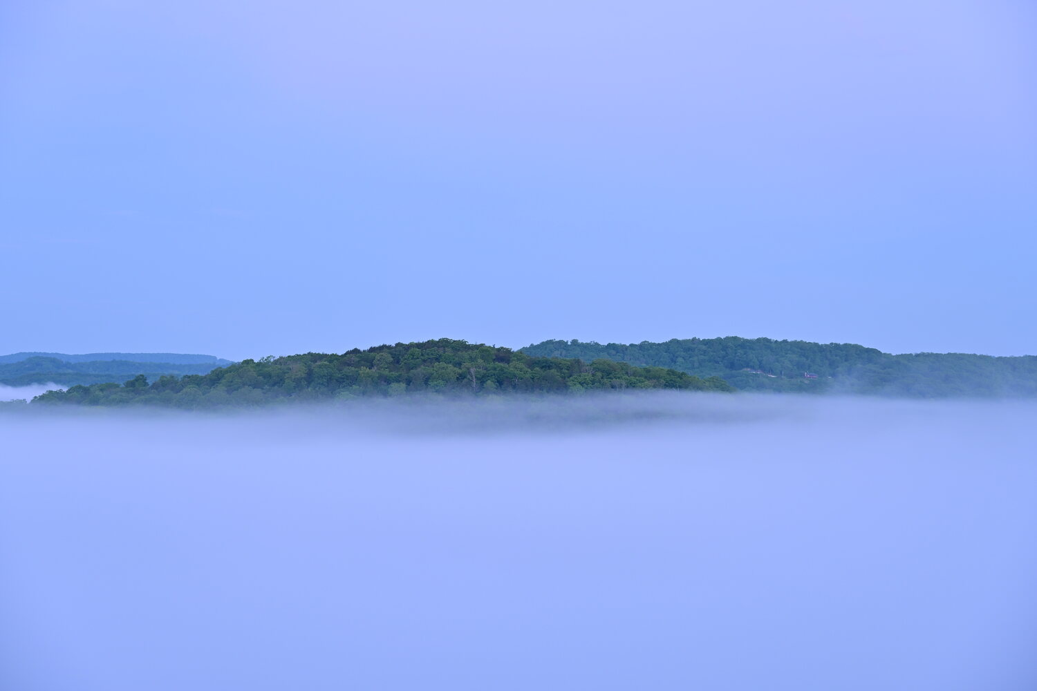 A forested hilltop rising like an island above a sea of morning fog over the White River valley