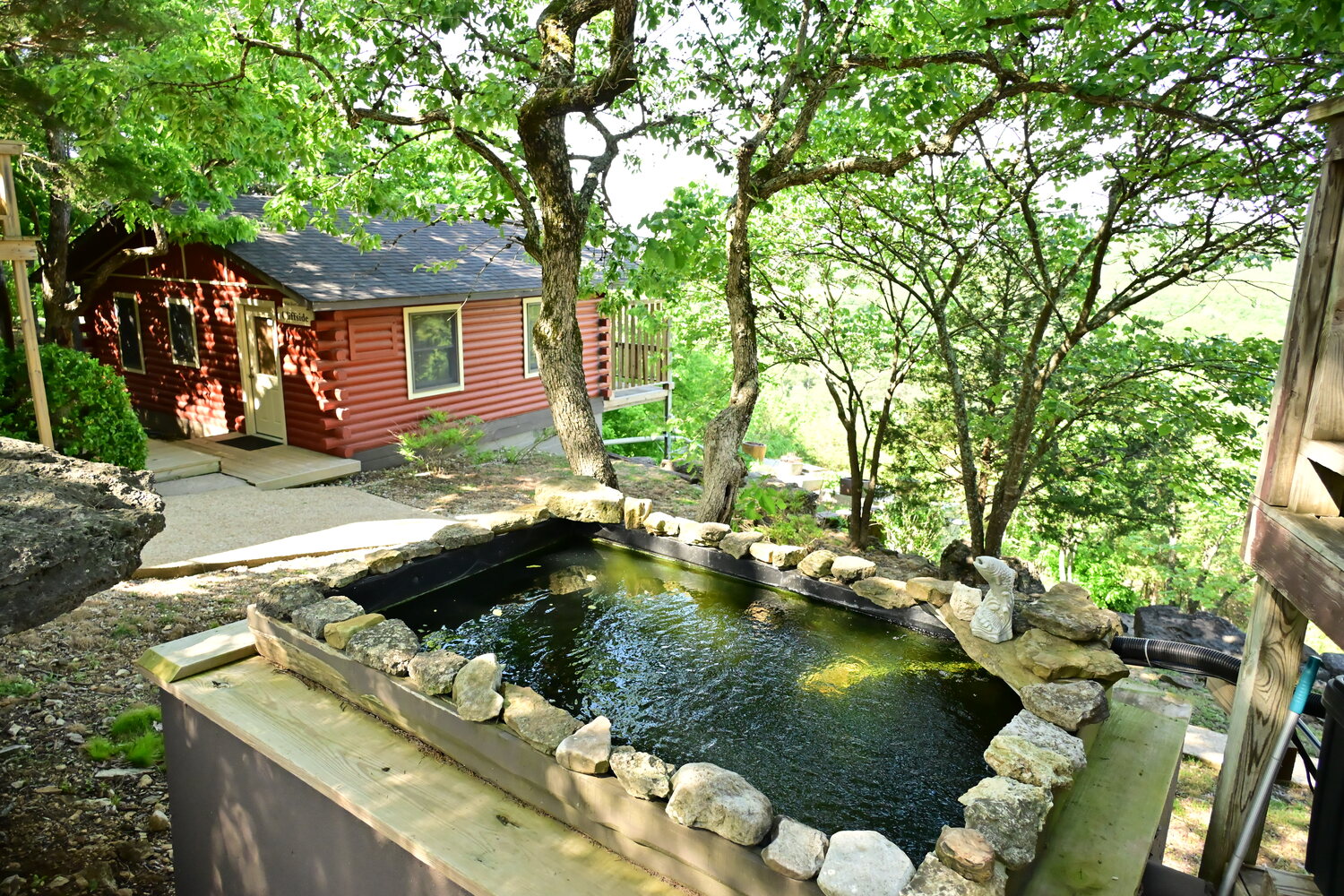 Stone koi pond water feature beside a red cabin on the property grounds
