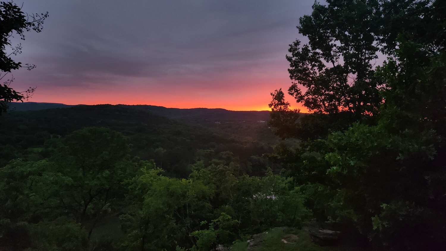 Pink and orange dusk sky over the forested Ozark hills surrounding White River Cabins