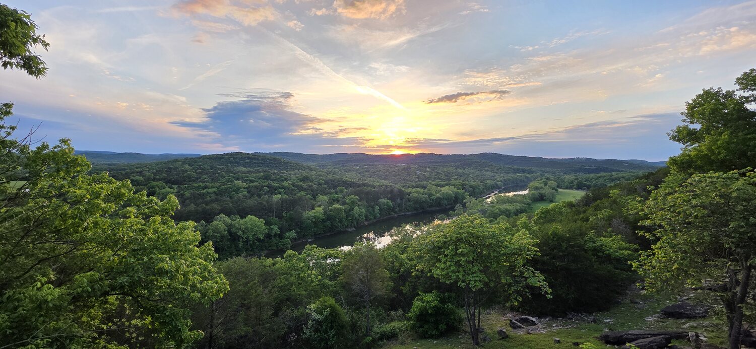 Golden sun setting over the green Ozark valley below the cliff-edge cabins